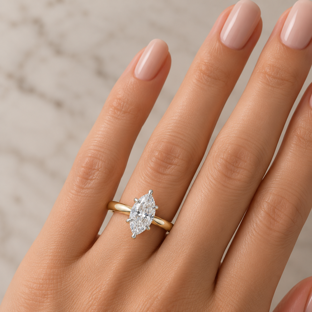 A close-up of a hand wearing a yellow gold ring with a marquise-cut clear gemstone. 