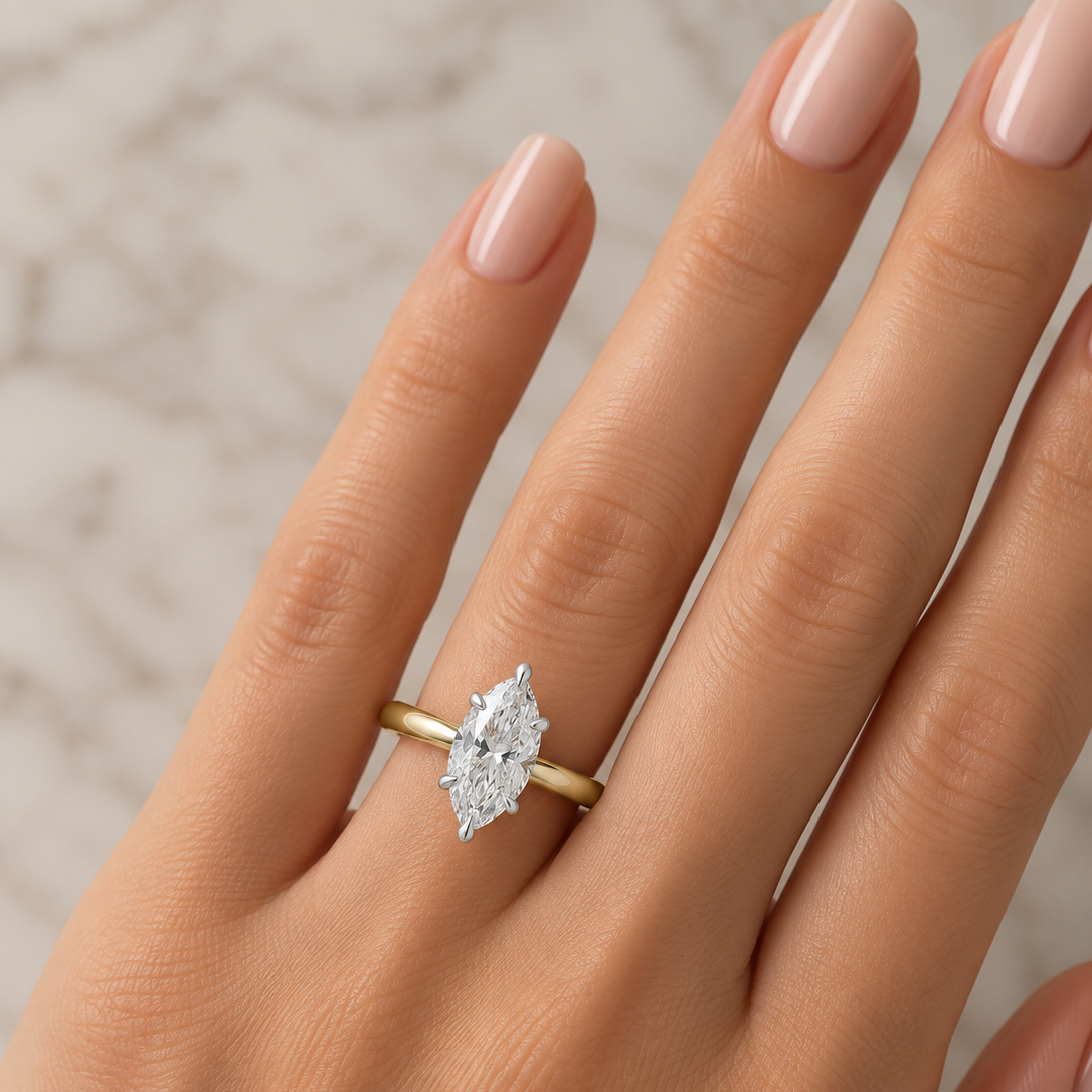 A close-up of a hand wearing a yellow gold ring with a marquise-cut diamond. 