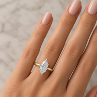 A close-up of a hand wearing a yellow gold ring with a marquise-cut diamond. 